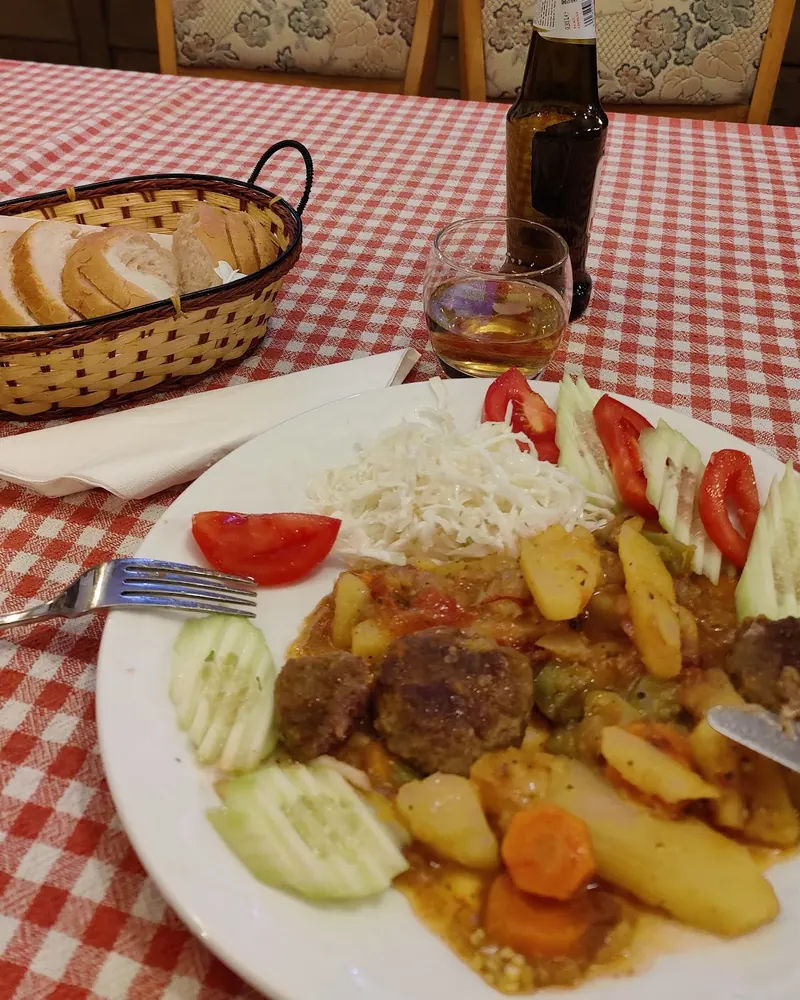 A home-cooked dinner plate of stew with meatballs, potatoes and fresh salad on a red gingham tablecloth