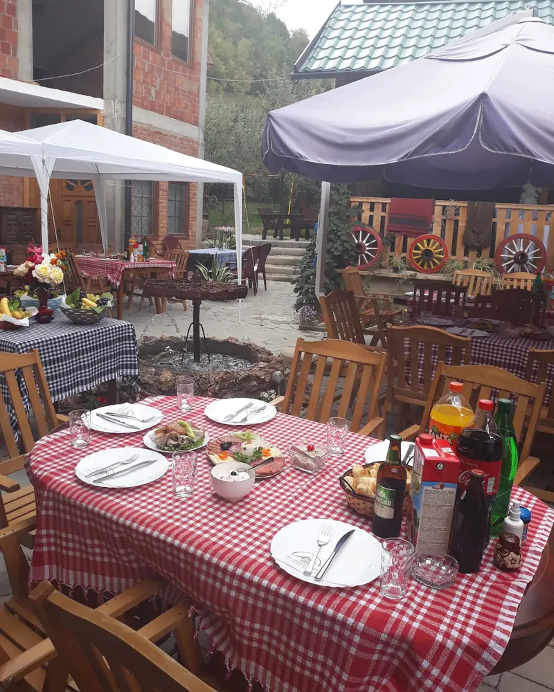 A table laid with gingham, plates and drinks in the garden under a parasol, with old cart wheels on the porch behind