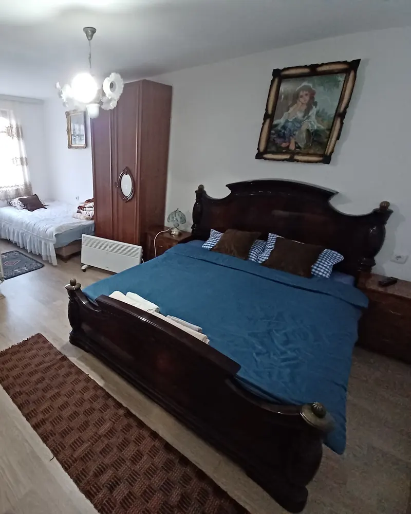 A large guest room with a carved dark-wood double bed, blue cover and a woven runner
