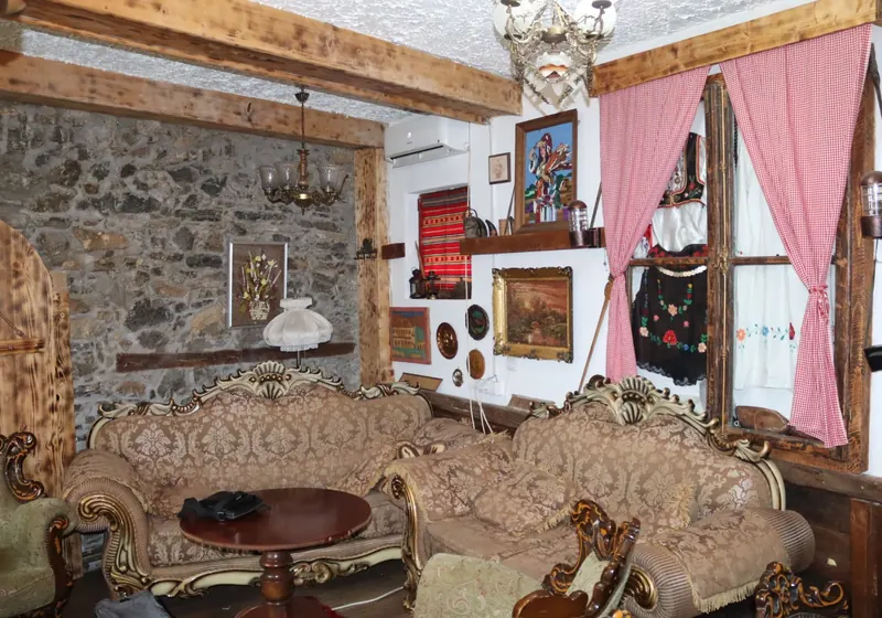The salon with antique carved sofas, a stone wall, pink gingham curtains and a folk costume on the wall