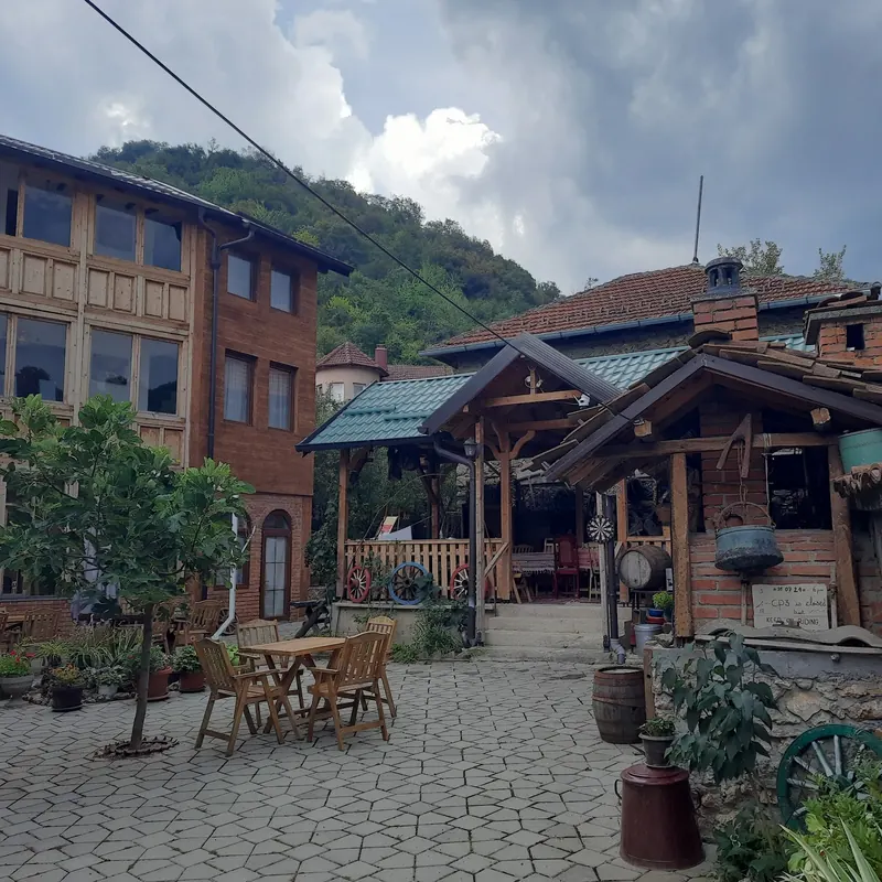 The courtyard with a wooden porch, brick chimney and green hills of the Sharr mountains behind