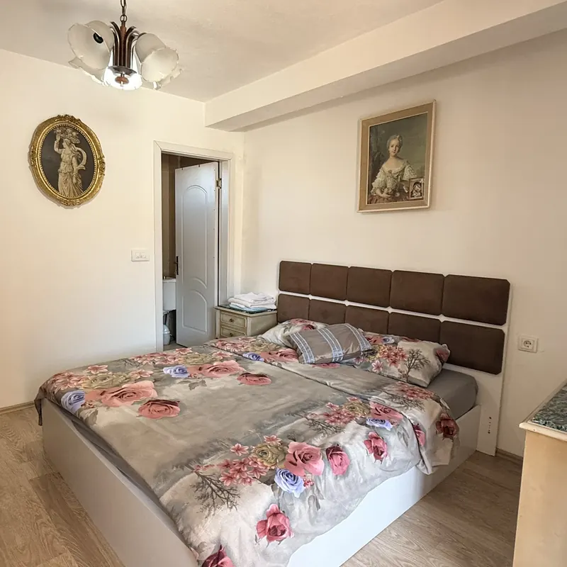 Bright double room with a rose-print cover, upholstered headboard and framed portraits